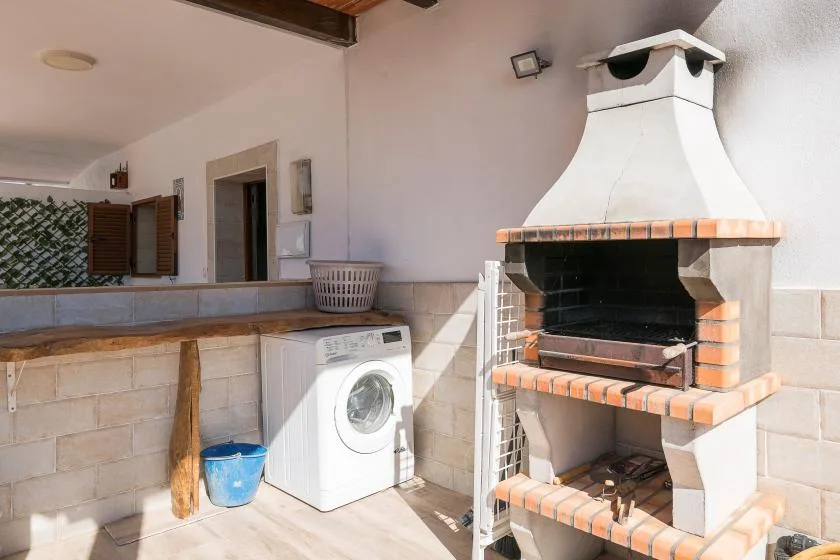 A tiled outdoor utility area with a washing machine and built-in barbecue.