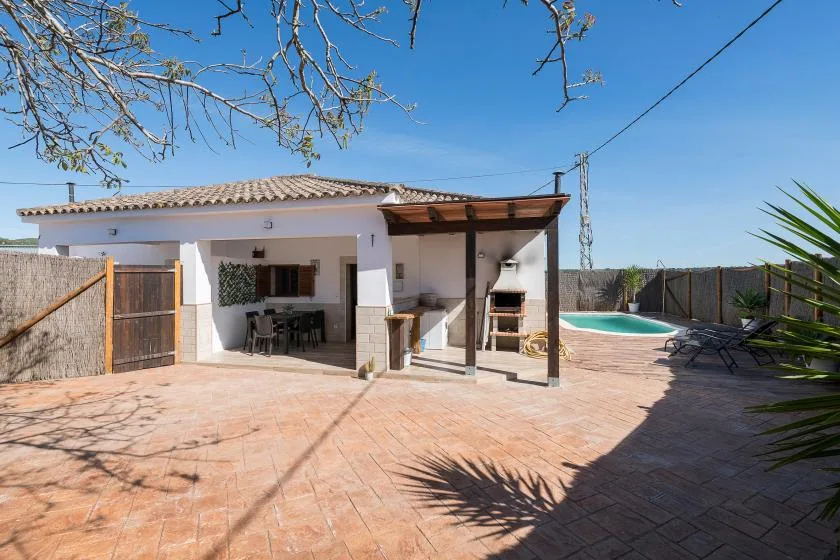 A paved outdoor patio with covered seating and a swimming pool.