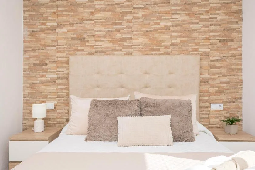 A bedroom with a bed, layered pillows, and a textured accent wall.