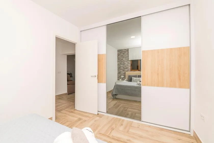 A bedroom with sliding mirrored wardrobe doors and light wood flooring.