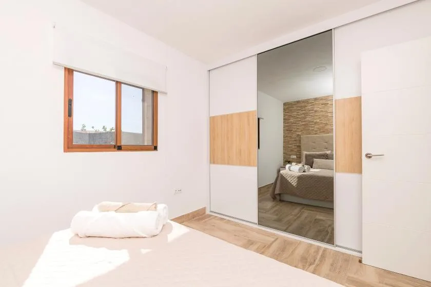 A bright bedroom with a bed and mirrored sliding wardrobe doors.