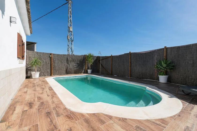 An outdoor swimming pool sits beside a tiled patio and a high privacy fence.