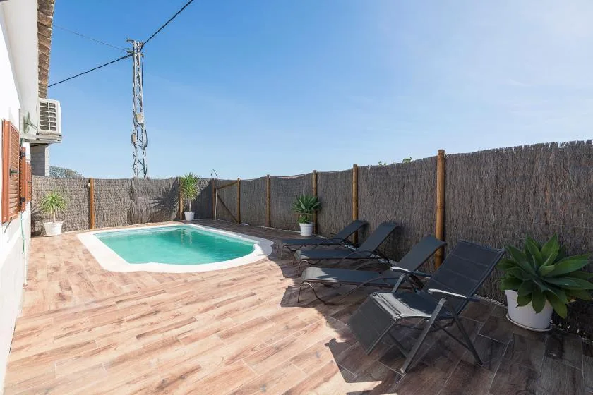 An outdoor pool and patio with lounge seating beside a privacy fence.