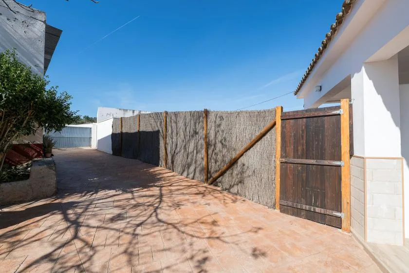 A paved outdoor passage runs beside a white building and a wooden gate.