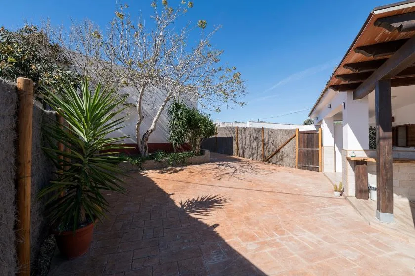 An outdoor paved courtyard with plants, a wooden gate, and a covered patio.