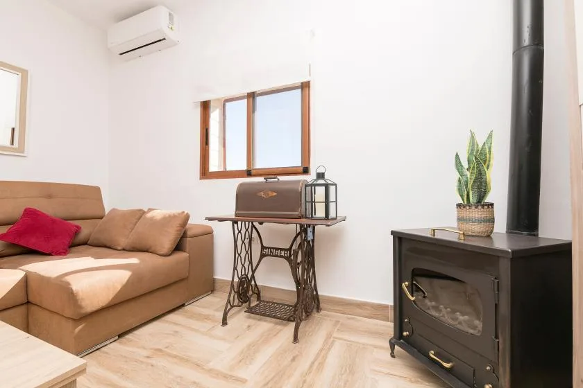 A bright living room with tan seating, a sewing machine, and a wood-burning stove.
