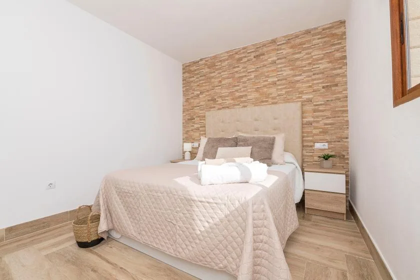 A bedroom with a neatly made bed against a textured accent wall.