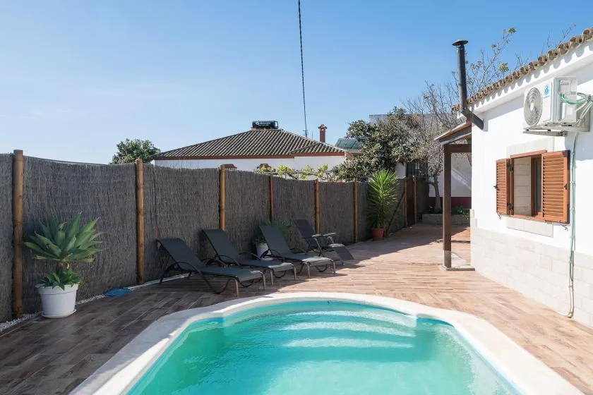 A sunny outdoor pool area with lounge seating beside a white building.