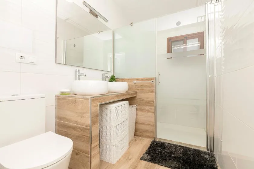 A bright bathroom with a vanity, vessel sinks, and a glass shower.
