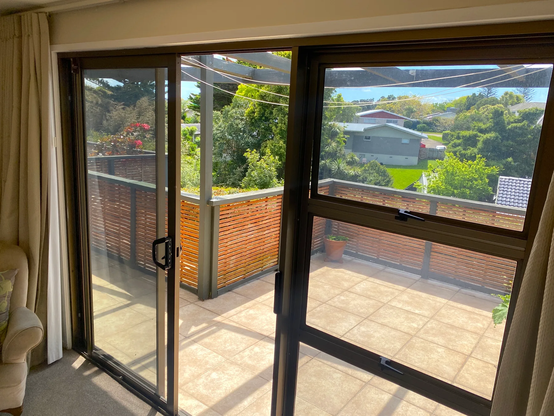 Sliding glass doors open onto a sunlit tiled balcony overlooking greenery.