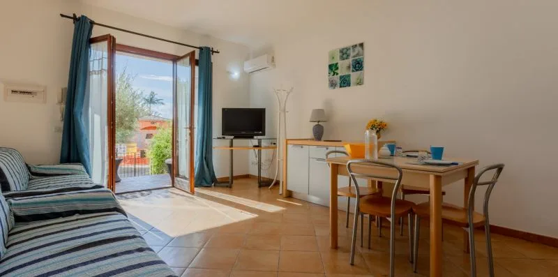 Una luminosa sala de estar y comedor con mesa, asientos y puertas abiertas al balcón.