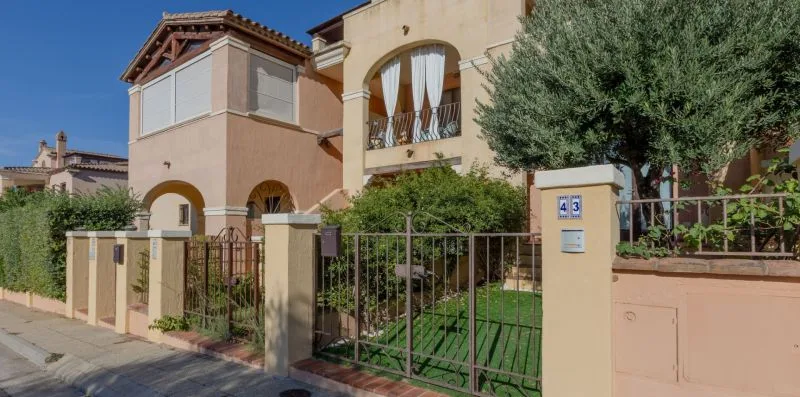 Una casa de estilo mediterráneo se encuentra detrás de una verja metálica y un jardín delantero.