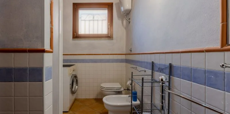 Un baño alicatado con inodoro, bidé y una ventana pequeña.