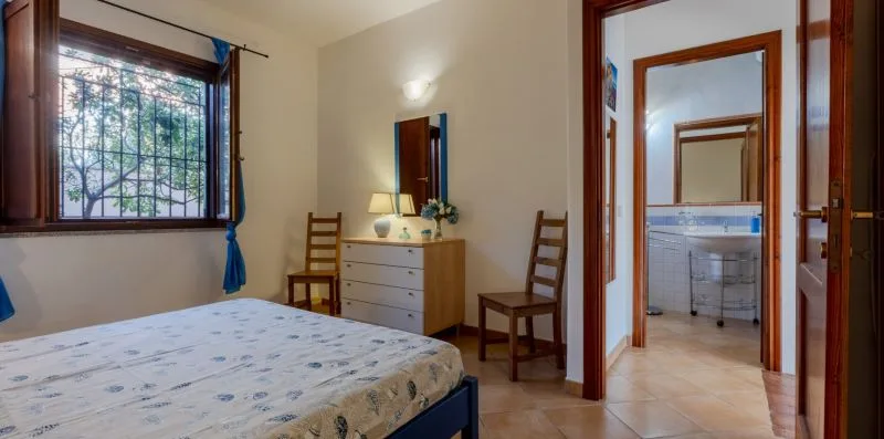 Un dormitorio con una cama, dos sillas y una puerta abierta hacia un baño.