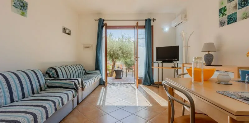 Una sala de estar con asientos a rayas, un televisor y una puerta de vidrio que da a un patio.