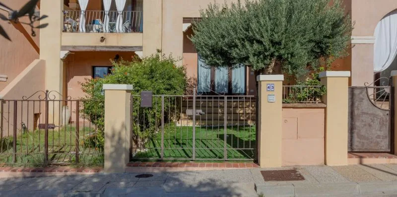 Una entrada residencial con portón, jardín y árboles detrás de la reja.