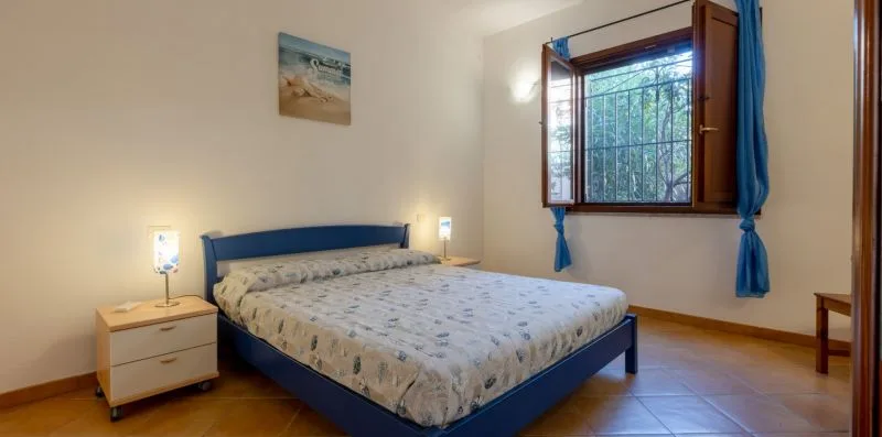Un dormitorio con una cama y una ventana abierta enmarcada por cortinas azules.
