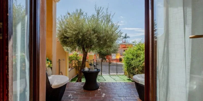 Un patio enmarcado por puertas abiertas, con un árbol en maceta y asientos al aire libre.