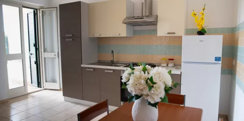 Una cocina con armarios, un refrigerador y un jarrón de flores sobre la mesa.