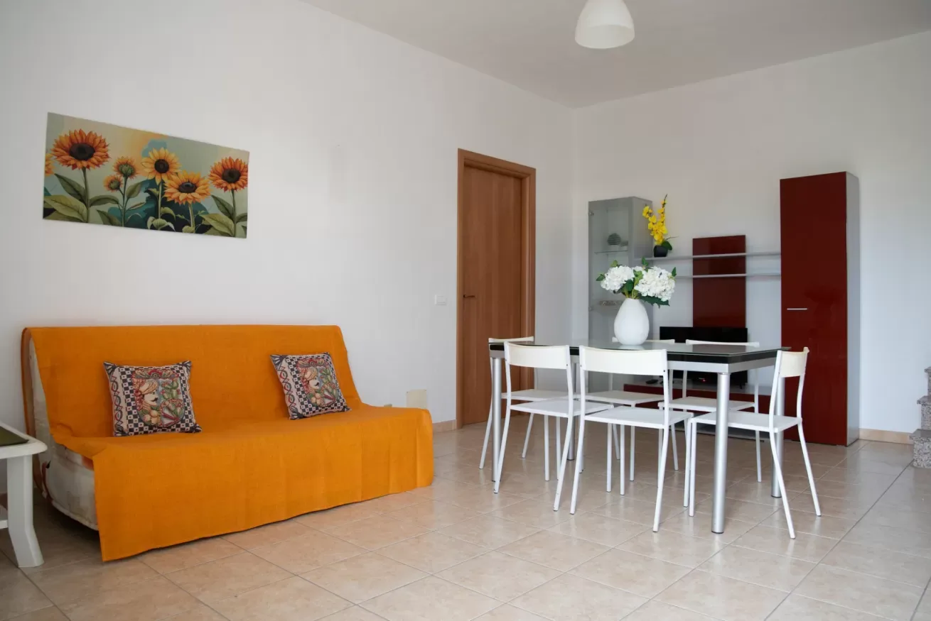 Una zona de comedor y estar con un sofá naranja y una mesa blanca con sillas.