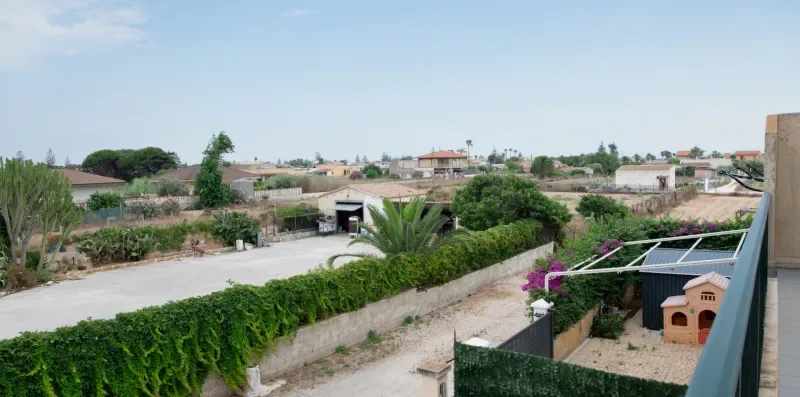 Una calle residencial junto a un seto, con casas y jardines al fondo.