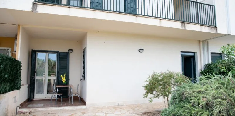 Un patio junto a un edificio blanco, con asientos cerca de una puerta de cristal.
