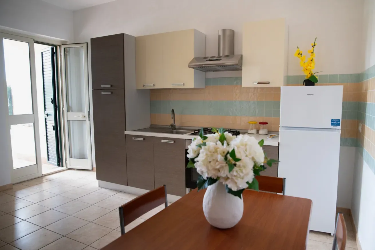 Una cocina con armarios, un refrigerador y una mesa de comedor con flores.