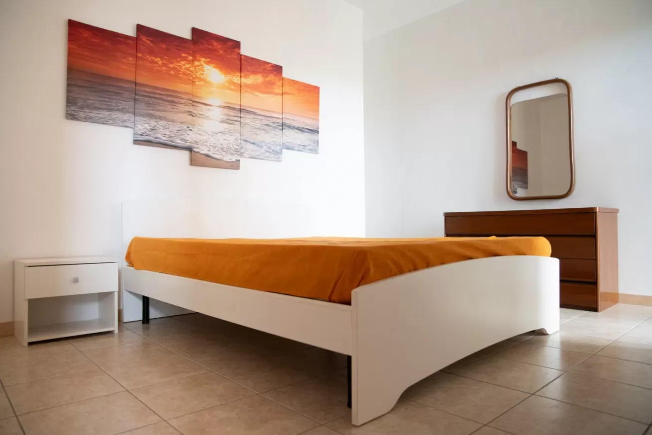 Un dormitorio con una cama cubierta con ropa de cama naranja y una imagen de atardecer en la pared.