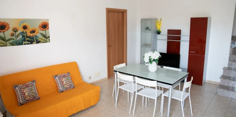Una luminosa sala de estar y comedor con una mesa, sillas blancas y un sofá naranja.