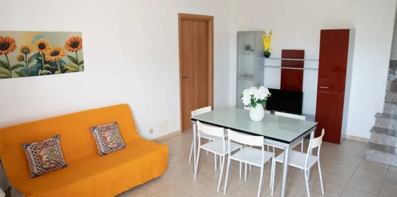 Una zona de comedor y estar con un sofá naranja y una mesa rodeada de sillas.