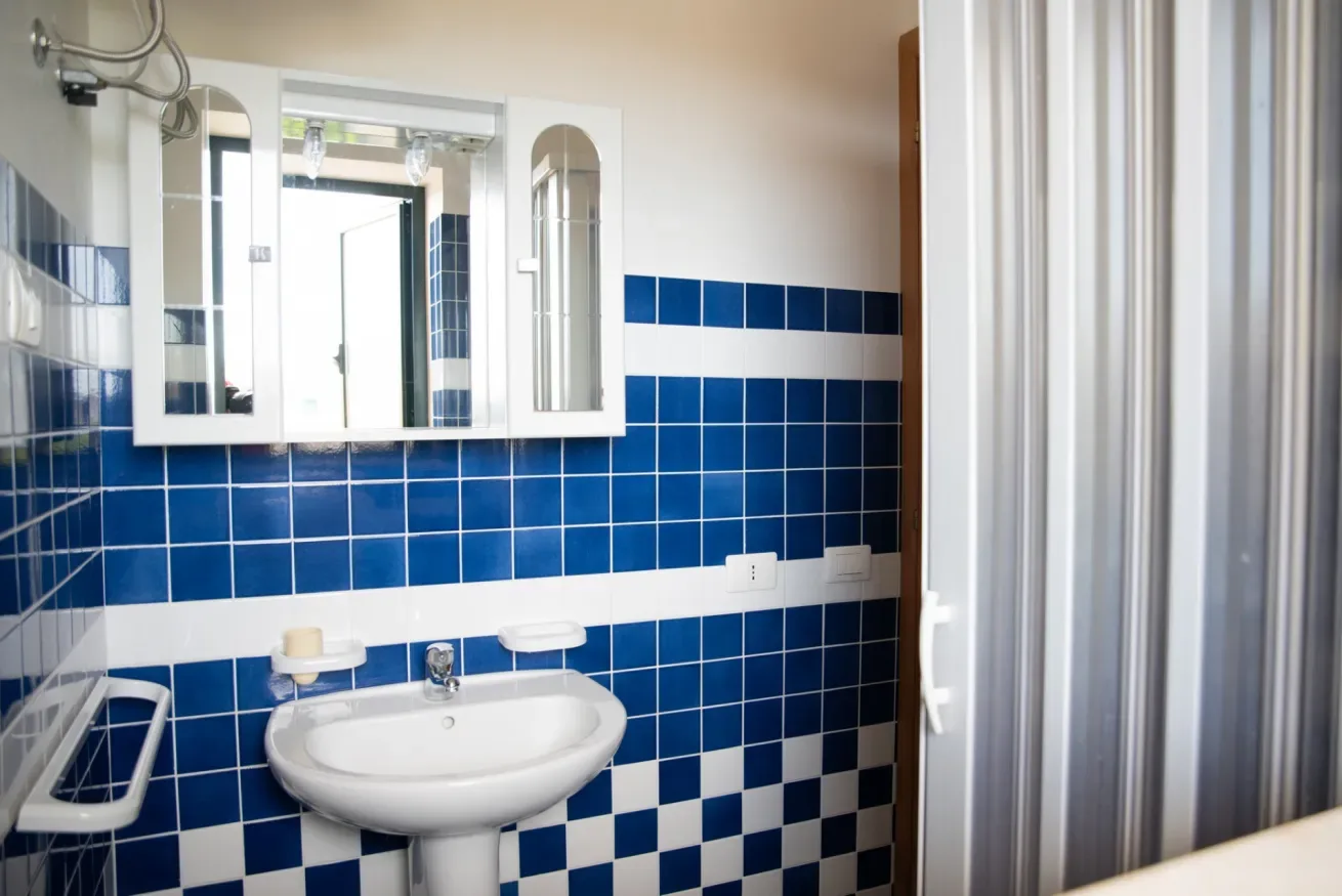 Un baño con paredes de azulejos azules y blancos y un lavabo bajo un armario con espejo.