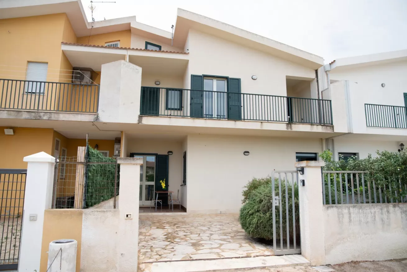 Un edificio residencial de tonos claros con balcones y una entrada pavimentada.