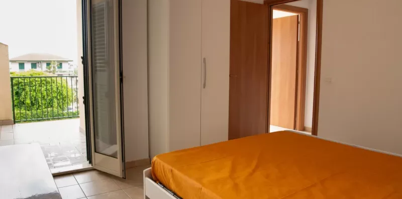 Un dormitorio con una cama naranja y una puerta abierta al balcón.