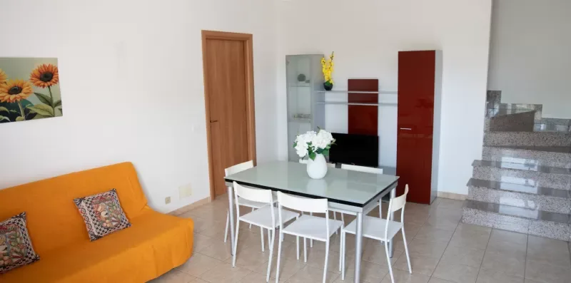 Una zona de comedor y sala de estar con una mesa de vidrio y asientos naranjas.
