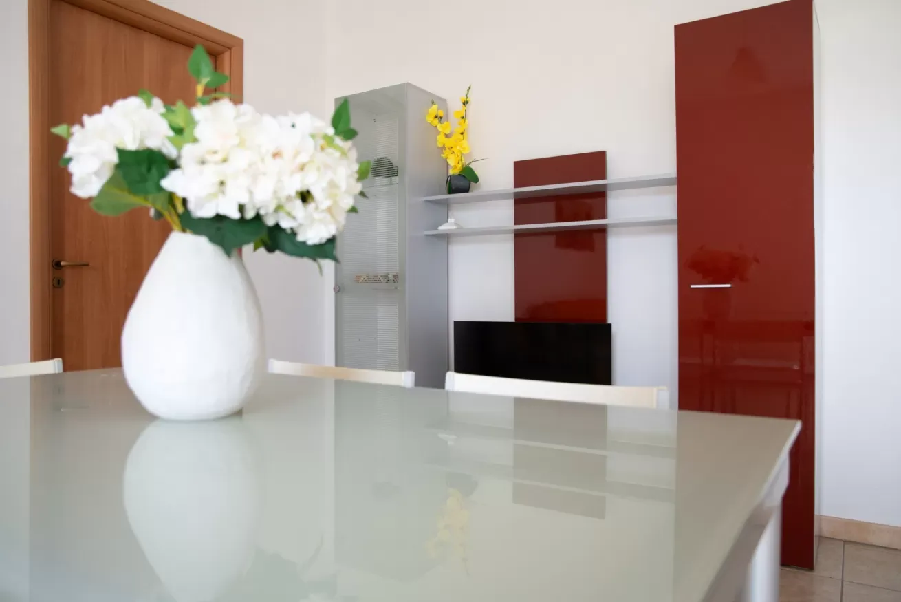 Una mesa de comedor con un jarrón de flores blancas está frente a un mueble de pared.
