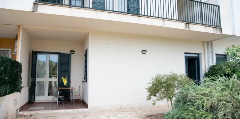 La entrada de un edificio da a un pequeño patio con asientos y plantas cercanas.