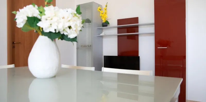 Un interior luminoso muestra una mesa de vidrio con un jarrón de flores blancas.