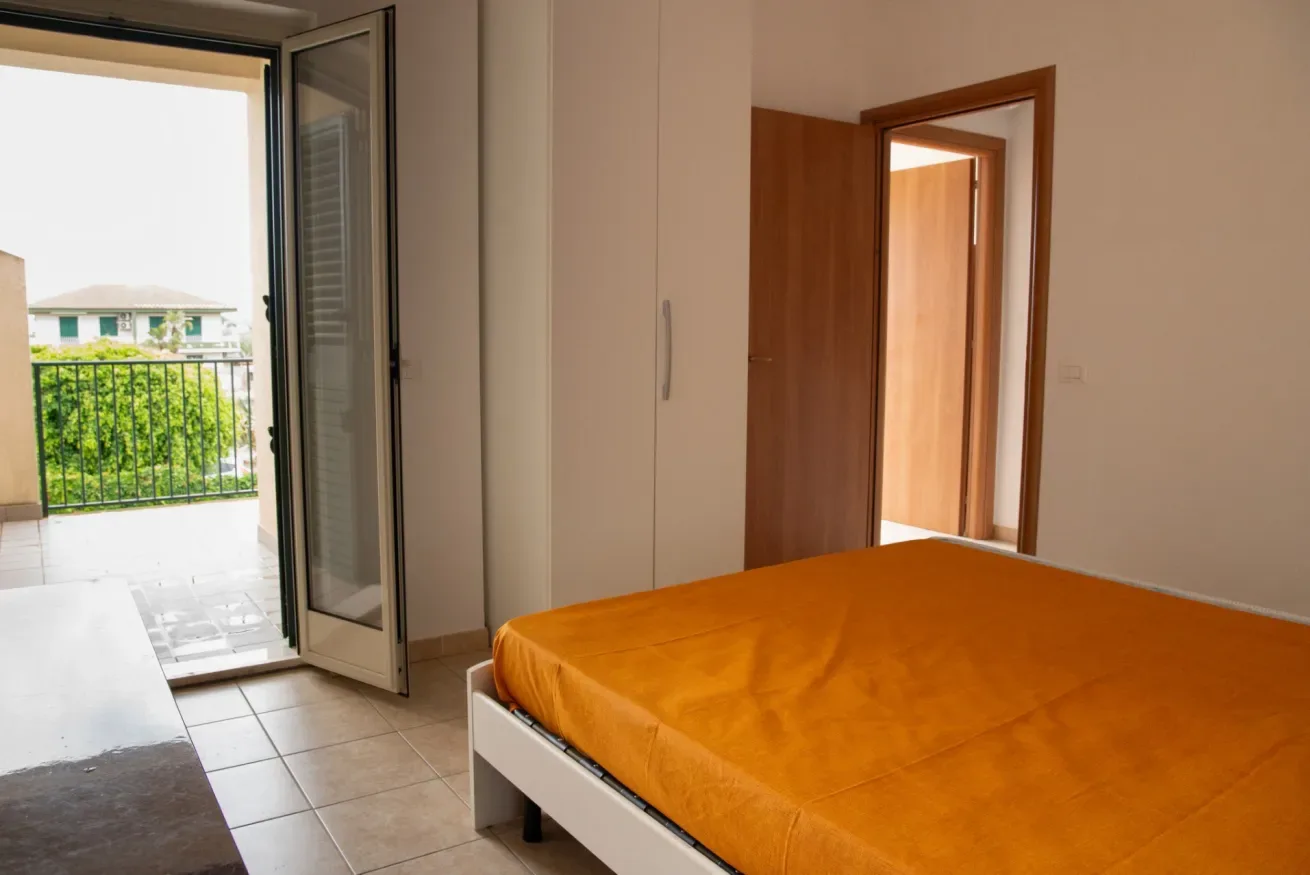 Un dormitorio con una cama naranja junto a una puerta abierta al balcón.
