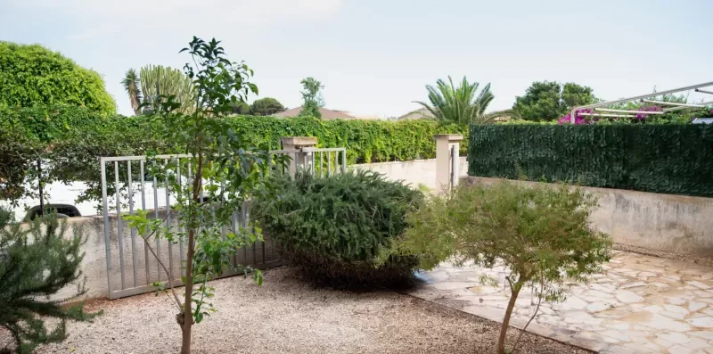 Entrada de jardín con una puerta metálica, arbustos y un camino de piedra.