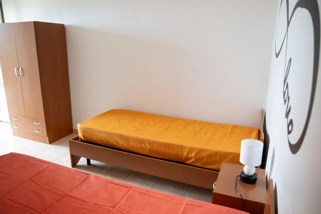 Un dormitorio con una cama cubierta de naranja, un armario y una mesita de noche.
