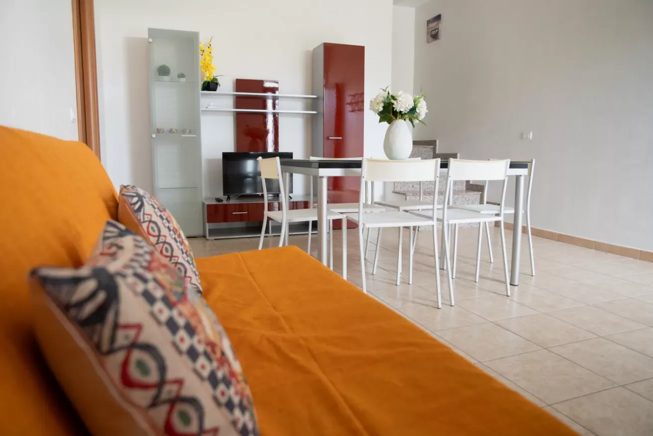 Comedor con una mesa y sillas blancas junto a un sofá naranja.