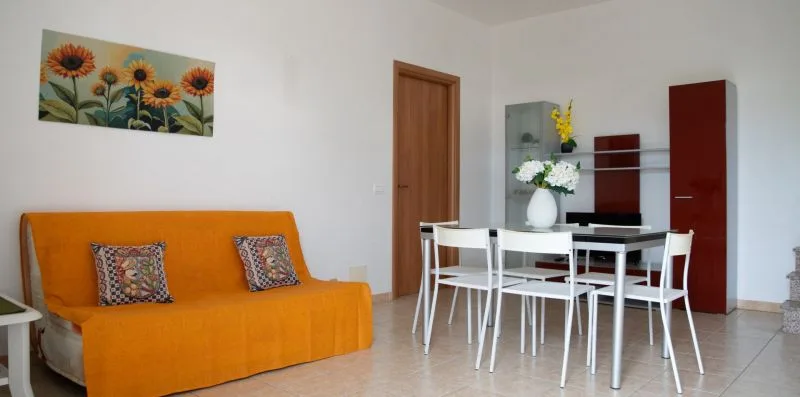 Zona de comedor y estar con asientos naranjas y una mesa blanca.