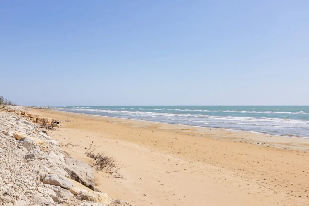 Una playa de arena se extiende junto al mar azul bajo un cielo despejado.