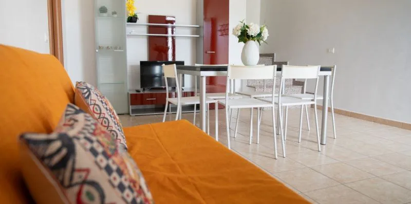 Una luminosa zona de comedor y estar con mesa, sillas y asientos naranjas.