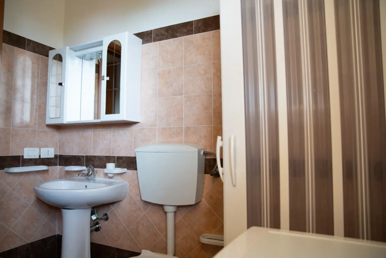 Un baño con azulejos, lavabo, inodoro y cortina de ducha a rayas.