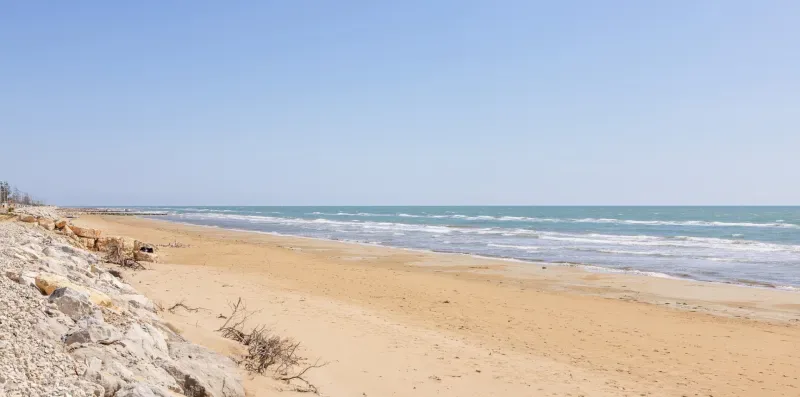Una playa de arena se extiende junto al océano, con olas en la orilla.