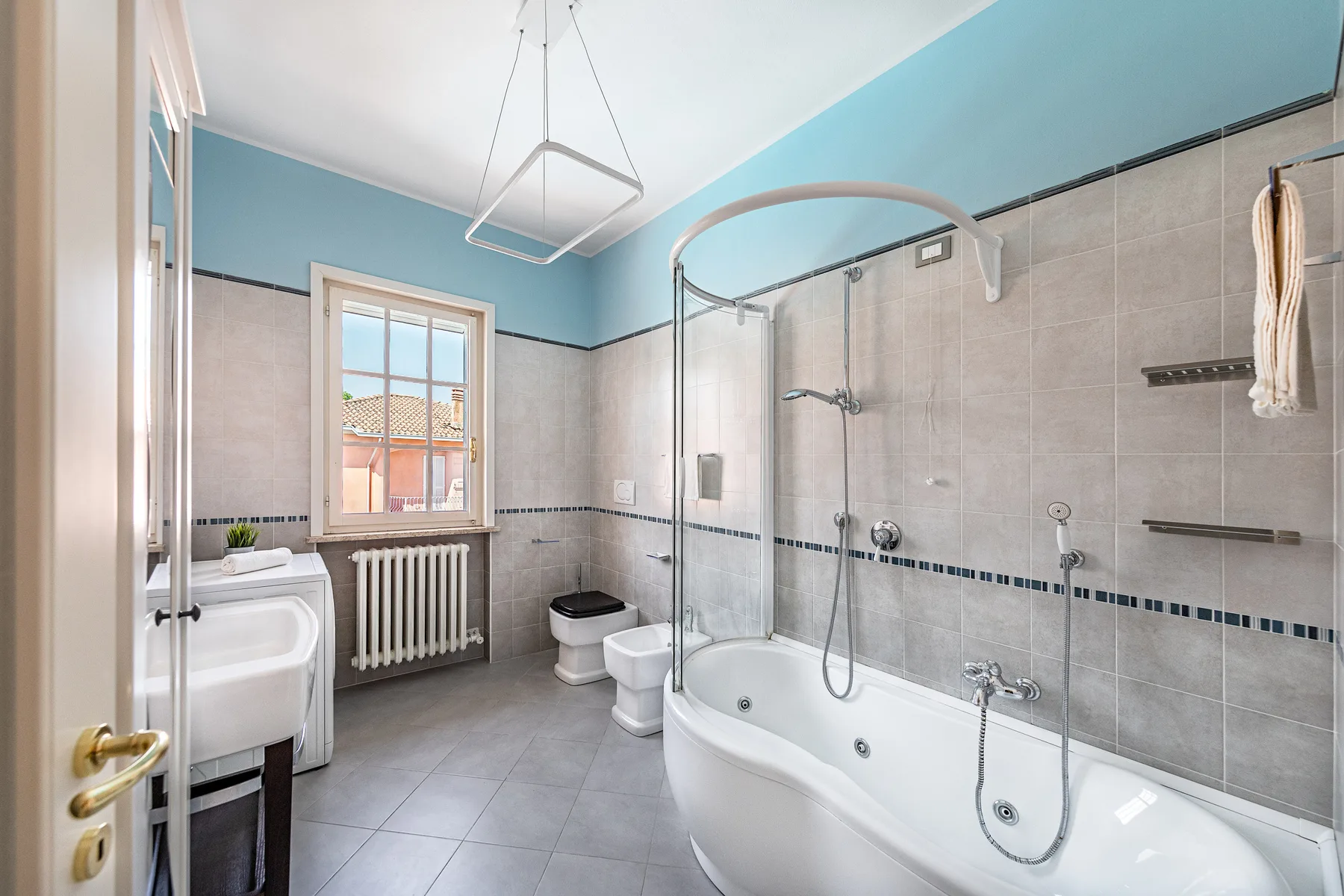 A tiled bathroom with a bathtub, shower, sink, and window.