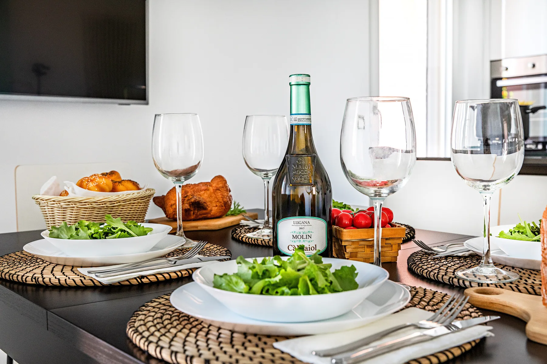 A dining table is set with salads, bread, wine glasses, and a bottle.