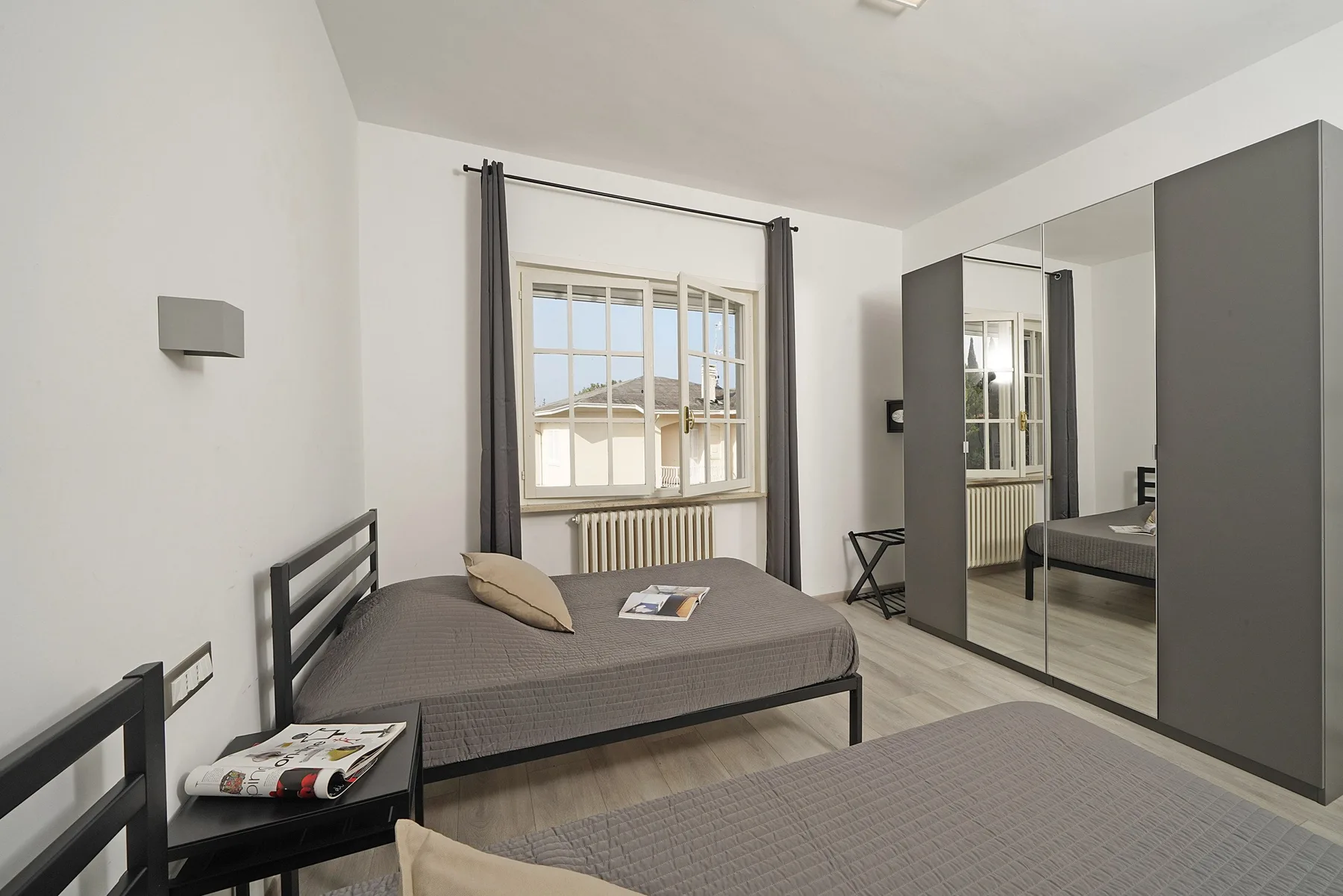 A bedroom with two beds and a mirrored wardrobe beside a window.