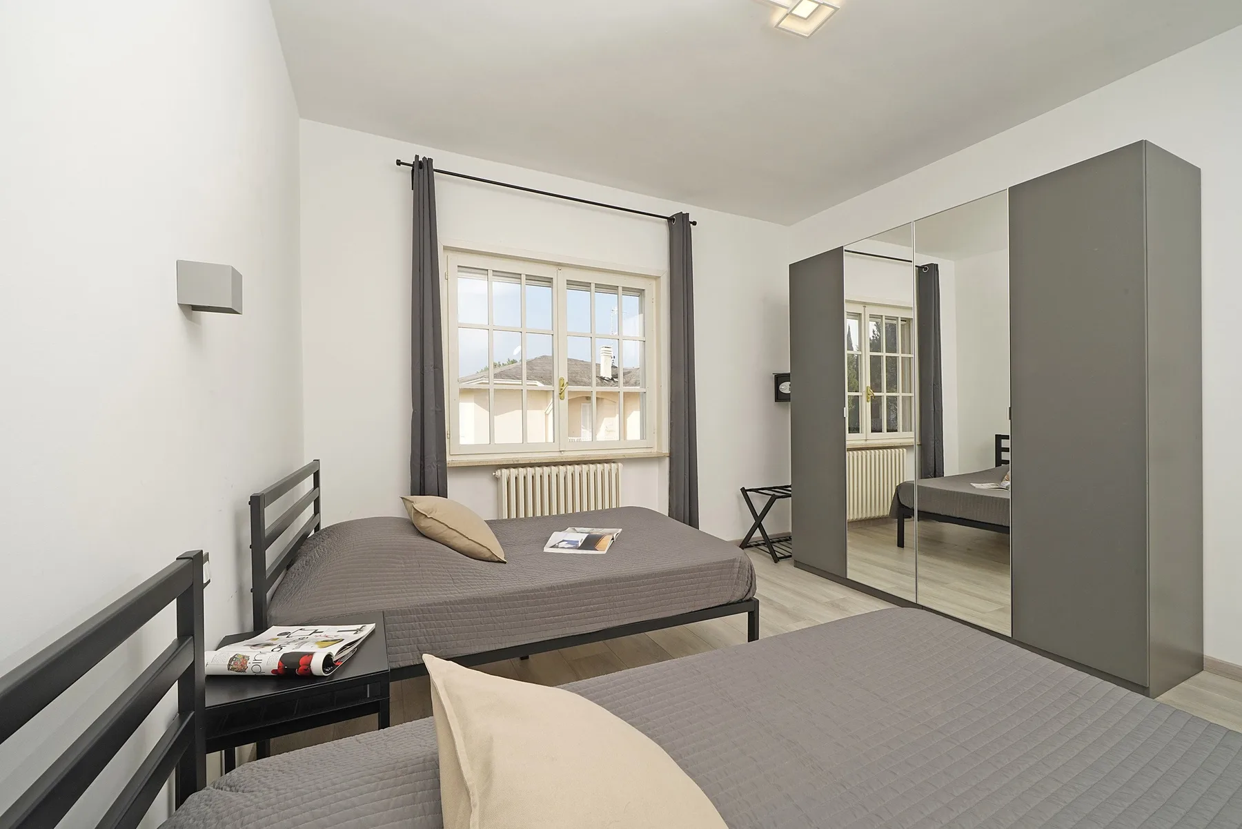 A bright bedroom with two beds, a window, and a mirrored wardrobe.